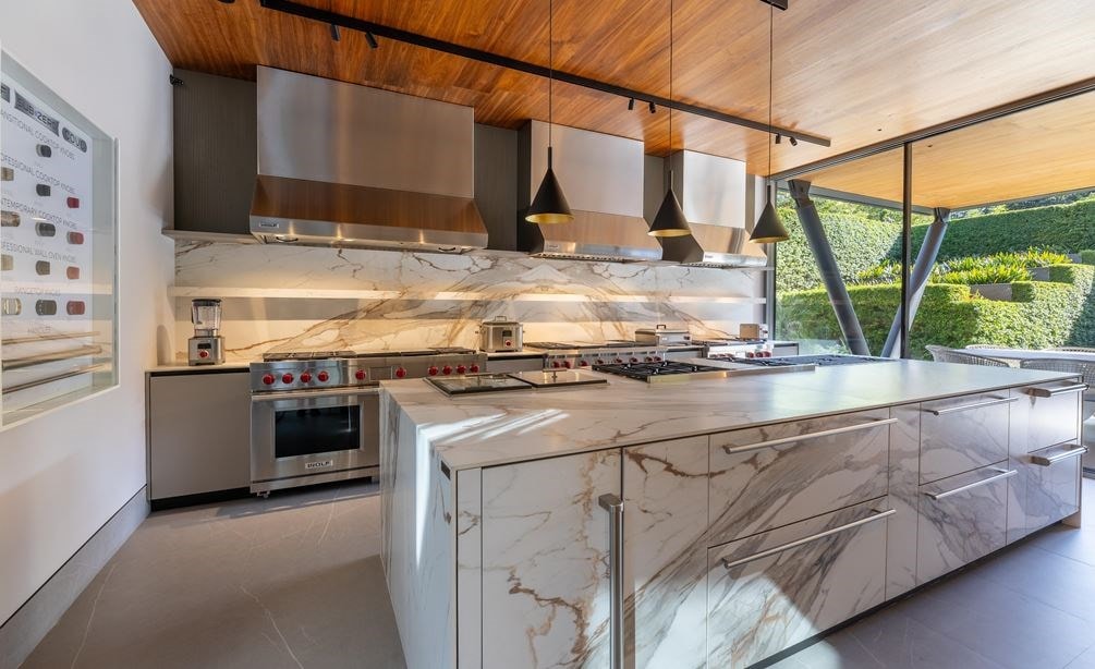 A luxury kitchen with granite countertops and a view to the outside patio featuring Wolf cooktops, ranges, and hoods.