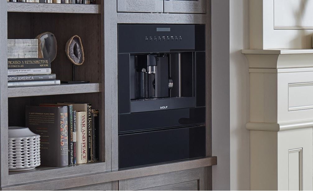 El sistema para café de vidrio negro de 24" Wolf (EC24/B) exhibido colocado a la perfección en una estantería con tonos cálidos de madera y manijas modernas