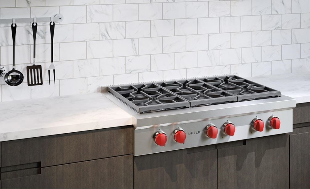 La estufa de 6 quemadores sellados de 36" Wolf (SRT366) brilla en este entorno clásico de cocina junto a gabinetes de panel plano y paredes de ladrillo blanco