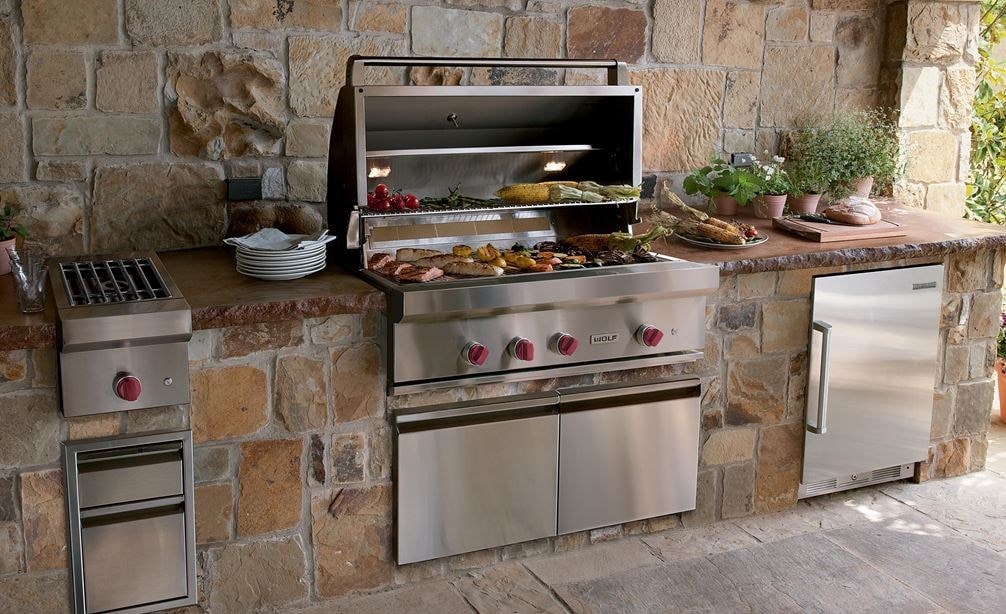 La parrilla de gas para exteriores de 42" Wolf (OG42) exhibida ofreciendo comodidades de cocina de última generación en un diseño de cocina para exteriores cálido y rústico.