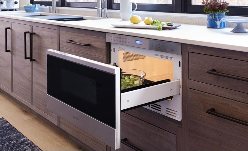 El cajón microondas transicional de 24" Wolf (MD24TE/S) agrega facilidad para la instalación al ras en gabinetes de madera cálida debajo de exhibidores blancos en cocinas modernas