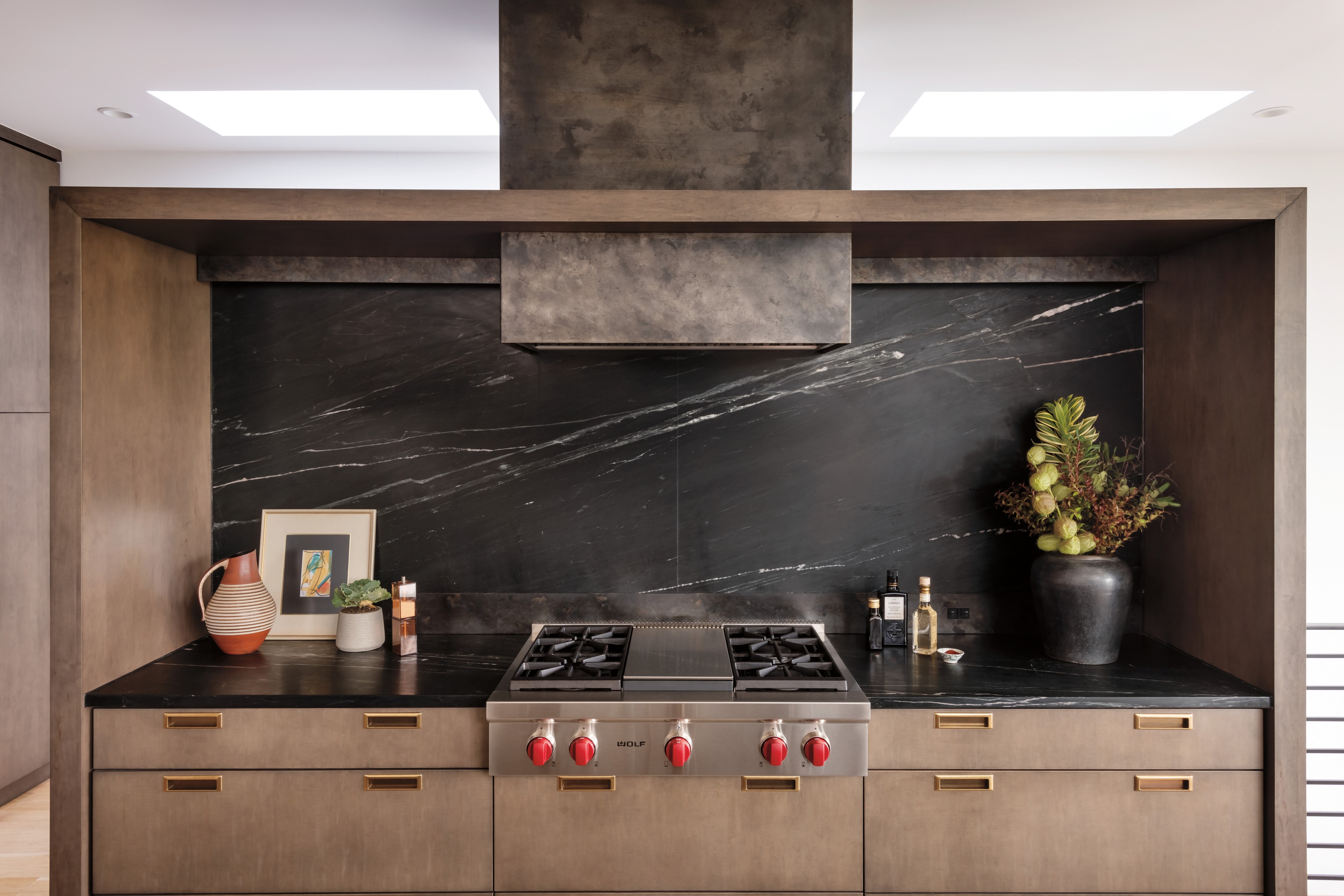 Estufa de 36" con 4 quemadores sellados y plancha infrarroja Wolf presentada en un diseño de cocina personalizada con gabinetes de madera natural y encimeras de granito oscuro con salpicadero a juego