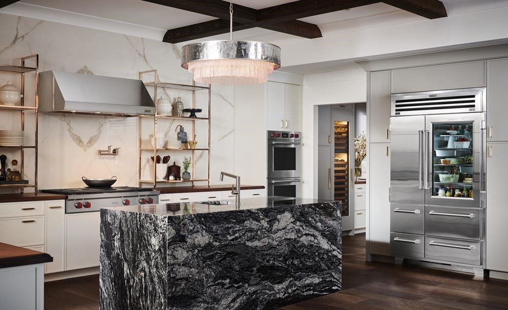 Refrigerador congelador Sub-Zero de 48" con puerta de cristal exhibido en un amplio diseño de cocina rústica de lujo, con encimeras y pisos en tonos de madera cálidos