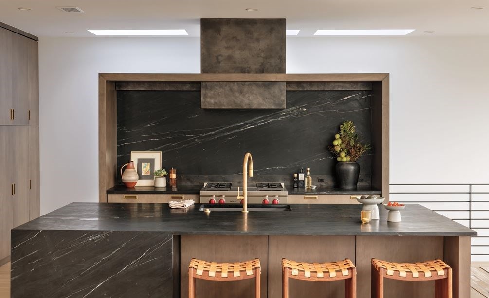 La estufa Wolf de 36" con cuatro quemadores sellados y plancha infrarroja, instalada en un espacio de madera personalizado con un salpicadero de mármol oscuro y una isla de cocina a juego