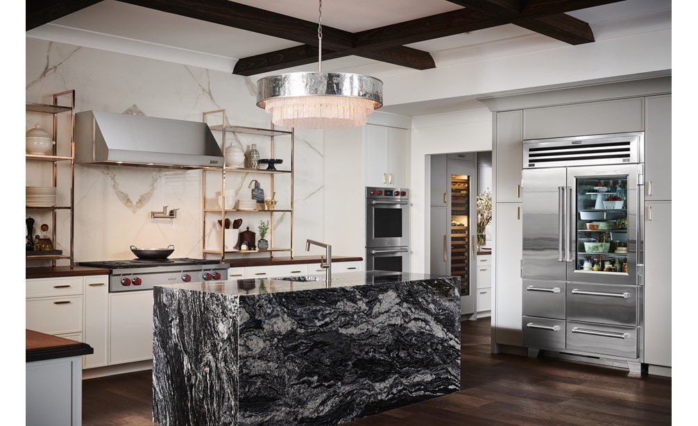 Refrigerador congelador Sub-Zero de 48" con puerta de cristal exhibido en un amplio diseño de cocina rústica de lujo, con encimeras y pisos en tonos de madera cálidos