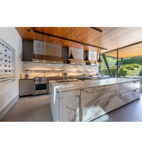 A luxury kitchen with granite countertops and a view to the outside patio featuring Wolf cooktops, ranges, and hoods.