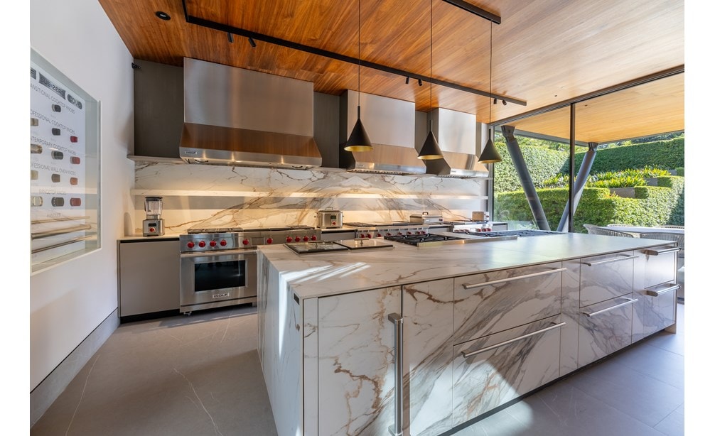 A luxury kitchen with granite countertops and a view to the outside patio featuring Wolf cooktops, ranges, and hoods.