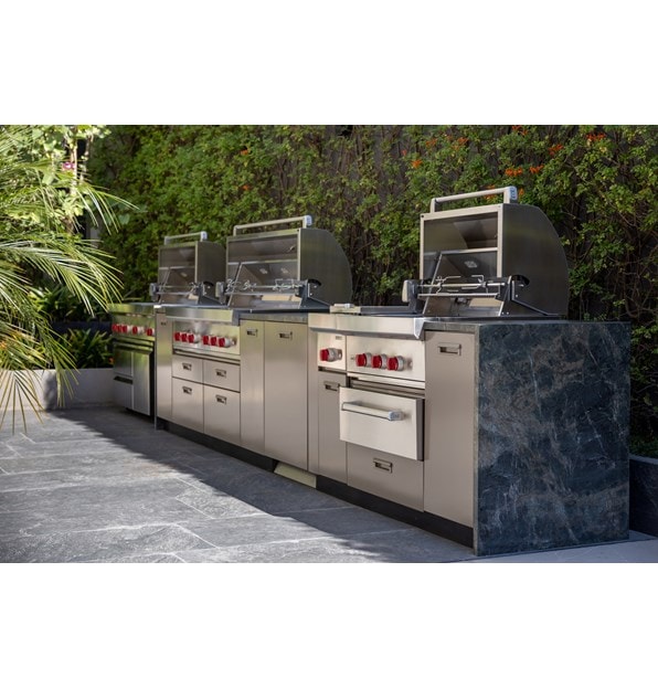 Three outdoor grills side-by-side a part of Wolf Appliances in front of a brush background.
