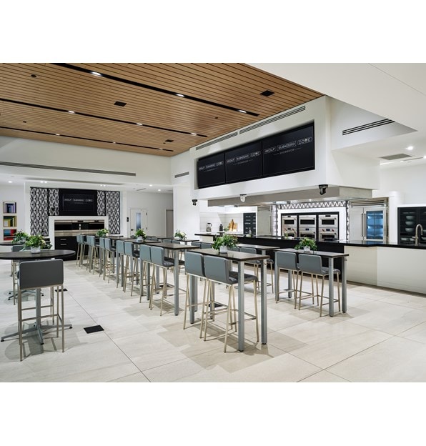 Built-In ovens by Wolf Appliances cover the walls next to a Sub-Zero refrigerator with blue-colored tall chairs.