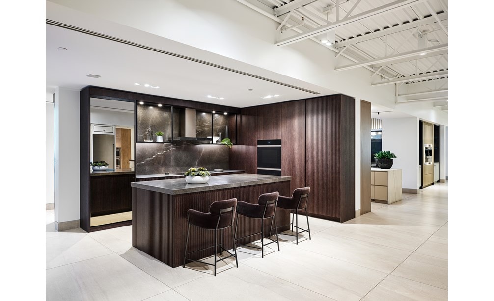 A brown and grey kitchen featuring brown chairs, a grey marble countertop and Wolf Appliance ovens.