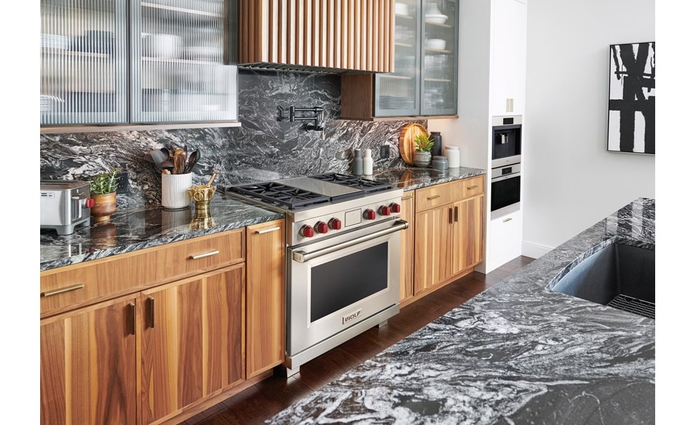 La estufa de energía dual de 36" Wolf exhibida en un moderno diseño de cocina de condominio con gabinetes personalizados y elegantes mostradores de mármol.