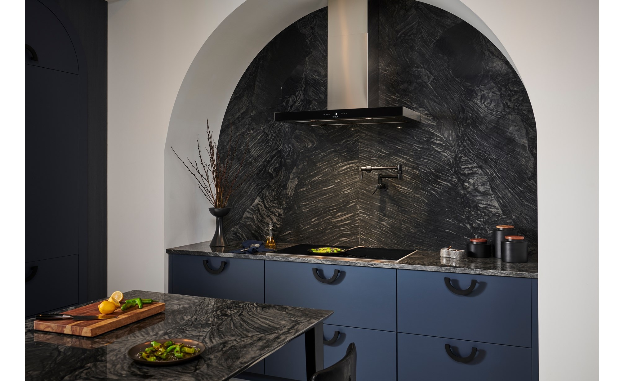 Placa de cocción con marco de transicional Wolf (CI365TF/S) exhibida en diseño de cocina arqueado personalizado con mostrador de mármol gris y salpicadero personalizado.