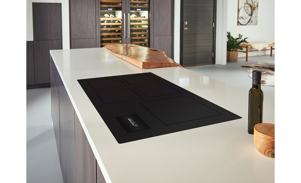 La placa de inducción contemporánea de 36" Wolf (CI36560C/B) presenta un diseño de cocina moderno, que se combina a la perfección con los mostradores blancos con gabinetes de tonos cálidos de madera.