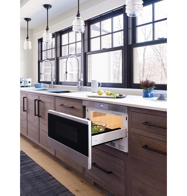 El cajón microondas transicional de 24" Wolf (MD24TE/S) agrega facilidad para la instalación al ras en gabinetes de madera cálida debajo de exhibidores blancos en cocinas modernas