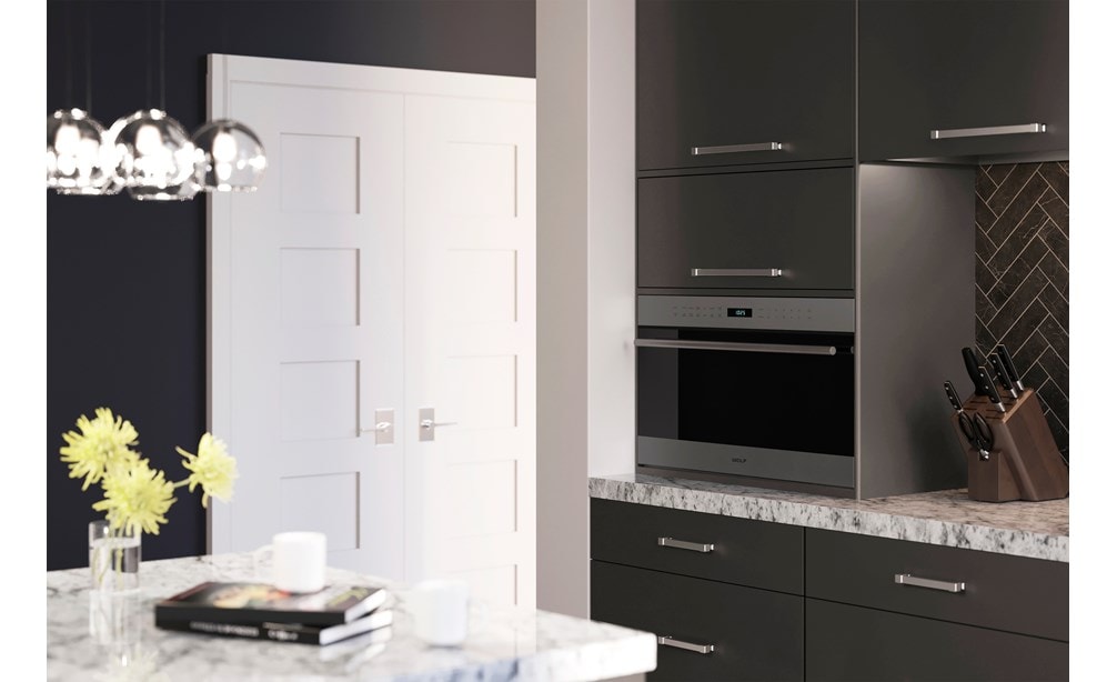 Horno microondas con puerta abatible transicional de 30" Wolf de la serie E (MDD30TE/S/TH) colocado de manera profesional en gabinetes lisos contra salpicaduras grises