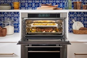 El horno de vapor con convección Wolf exhibido en una cocina de estilo mediterráneo con salpicaduras de azulejos azules y estantes de cocina abiertos.