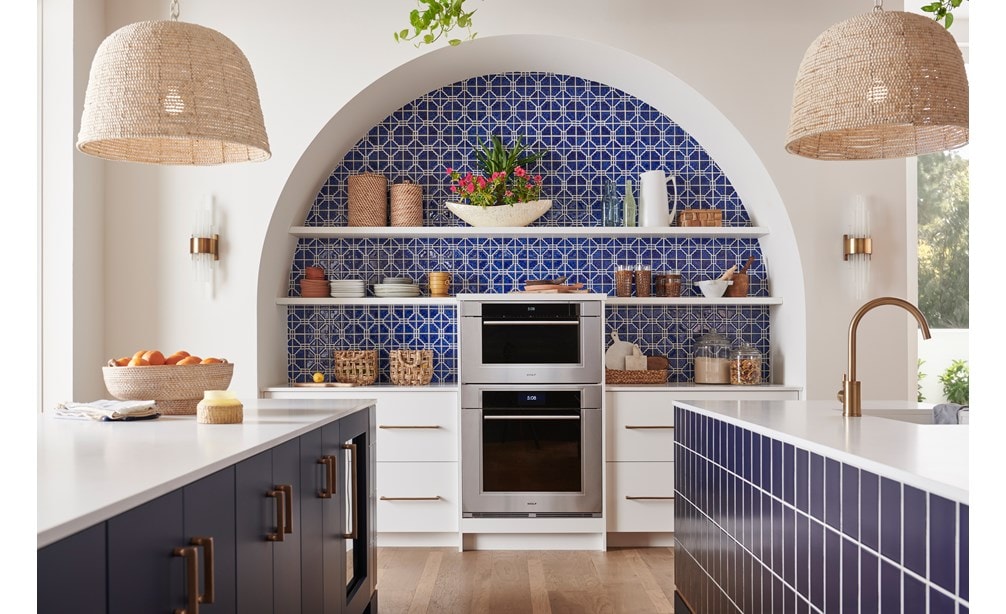 Wolf M Series Transitional Convection Steam Oven (CSO3050TM/S/T) shown in a bright and open Mediterranean kitchen design featuring blue mosaic tile backsplash, white open shelves, pendant lights and gold cabinet handles