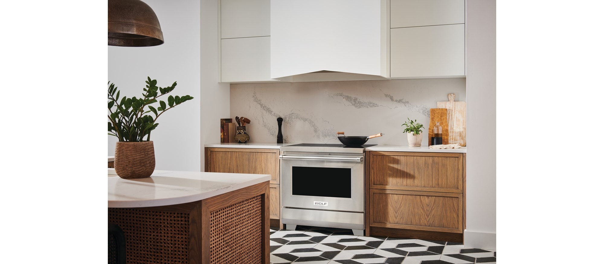 Estufa de inducción profesional de 36" y 34" Wolf (IR36550/S/P) con extractor de pared Wolf blanco presentada en cocina moderna con pisos de baldosas blancas y negras.