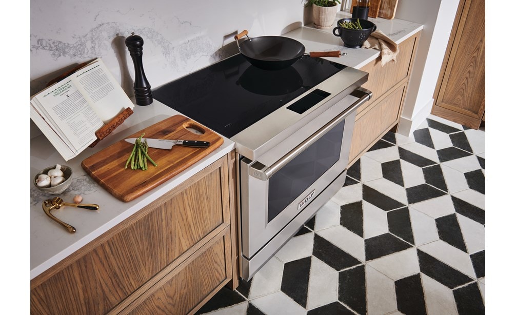 Estufa de inducción profesional de 36" y 34" Wolf (IR36550/S/P) con una sartén de wok en su superficie de cerámica negra junto a la tabla de cortar con espárragos.