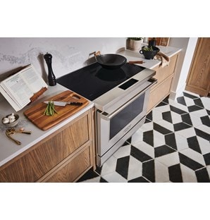 Estufa de inducción profesional de 36" y 34" Wolf (IR36550/S/P) con una sartén de wok en su superficie de cerámica negra junto a la tabla de cortar con espárragos.