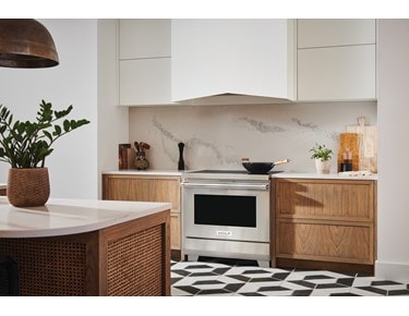 Estufa de inducción profesional de 36" y 34" Wolf (IR36550/S/P) con extractor de pared Wolf blanco presentada en cocina moderna con pisos de baldosas blancas y negras.