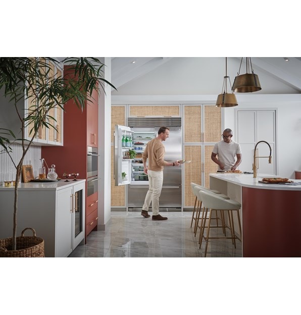 Dos hombres sonriendo mientras toman comida fresca de su refrigerador de acero inoxidable de la serie Classic de 48 pulgadas Sub-Zero