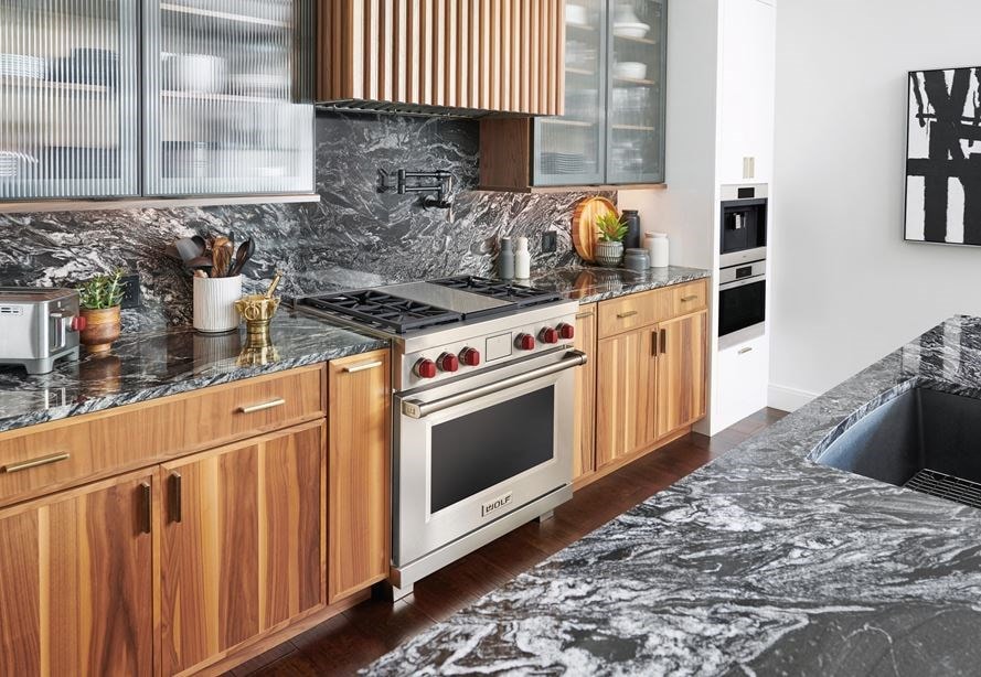 La estufa de energía dual de 36" Wolf exhibida en un moderno diseño de cocina de condominio con gabinetes personalizados y elegantes mostradores de mármol.