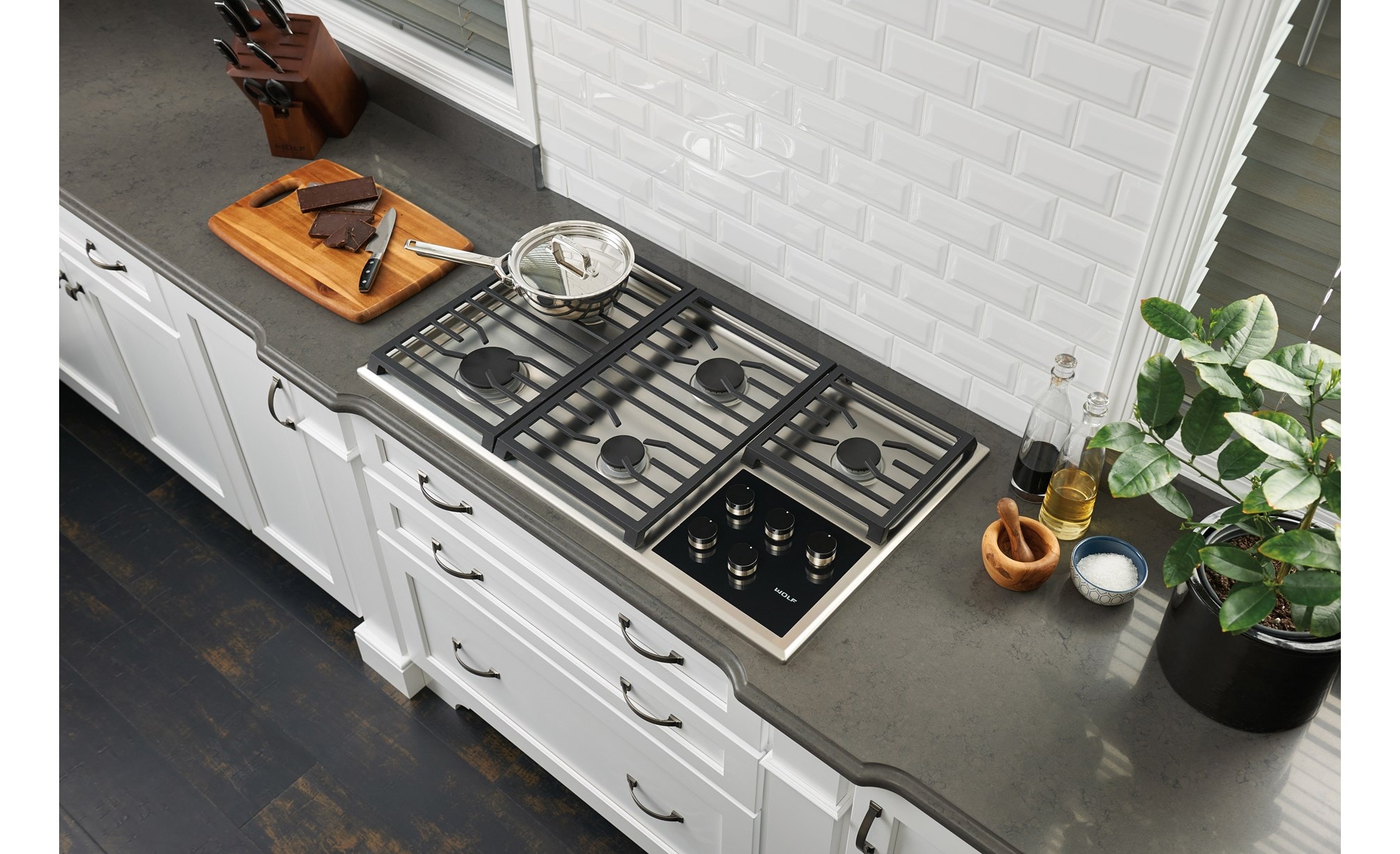 La placa de cocción de gas transicional de 36" Wolf con 5 quemadores (CG365T/S) centrada en un mostrador de granito liso y pulcro para un diseño de cocina clásico