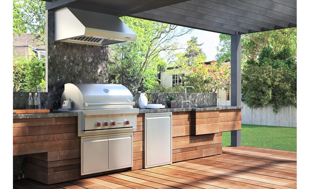 Parrilla de gas para exteriores de 36" Wolf (OG36) exhibida con campana de ventilación para exteriores profesional de Wolf en esta amplia cocina exterior. 