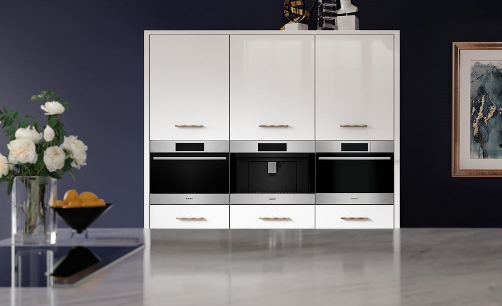 A Wolf built-in speed oven, coffee system, and a convection steam oven side-by-side in a white cabinet