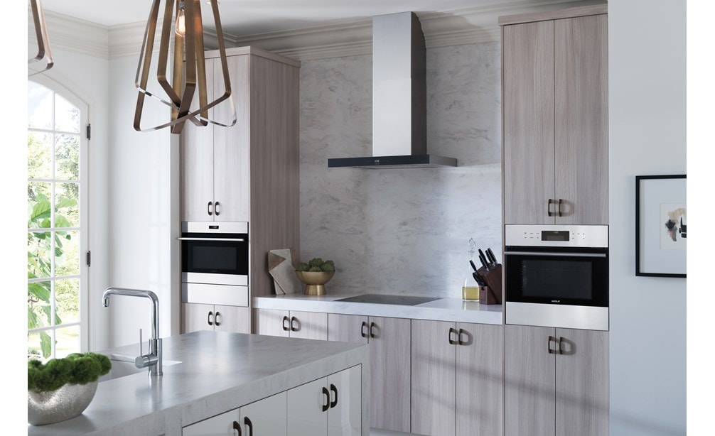 La campana extractora de placa de cocción de pared de 30" Wolf (VW30B) con placa de inducción de 24" Wolf (CI243C/B) exhibida en una amplia y luminosa cocina