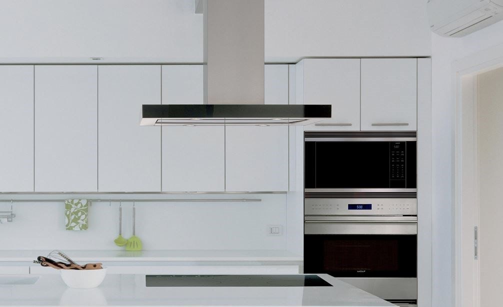 La campana extractora de placa de cocción para isla de 42" Wolf en negro (VI42B) exhibida combinándose a la perfección en un diseño de cocina lineal blanco con gabinetes sin manijas