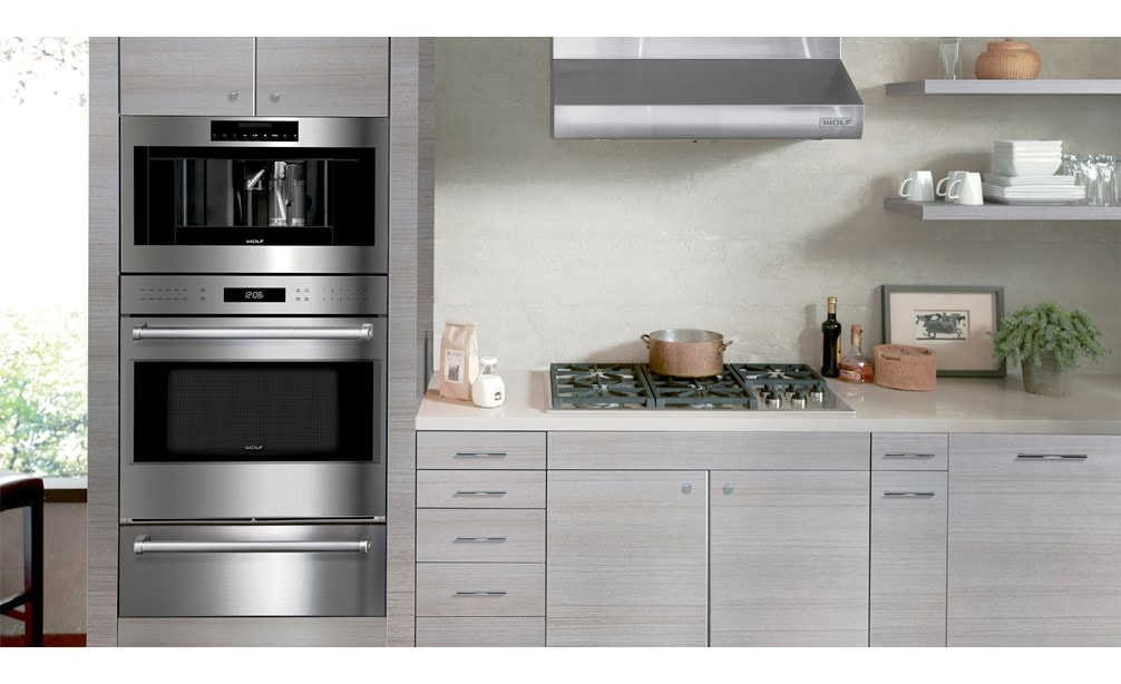 La campana extractora de pared de perfil bajo de 30" Wolf (PW302210) exhibida en un diseño de cocina limpio, compacto y potente con electrodomésticos Wolf de la mejor calidad